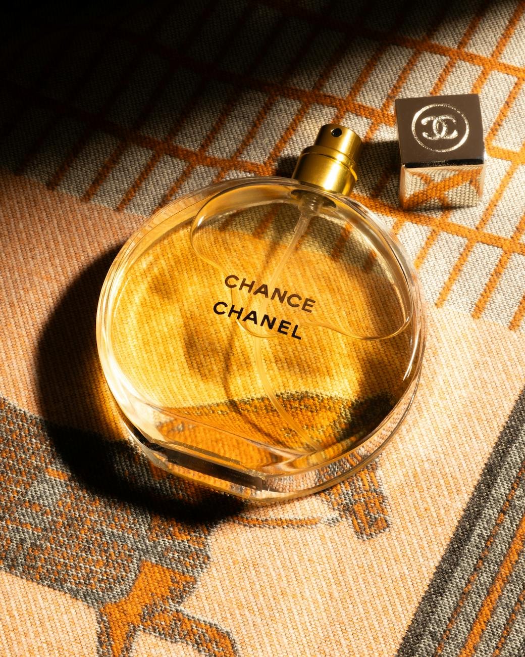 Elegant glass bottle of Chanel Chance fragrance with branded cap on textured fabric.